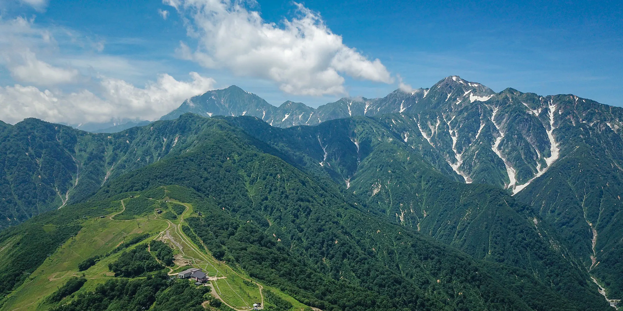 Aerial view over the Happo-one ridge toward the snow-streaked peaks of Hakuba Sanzan