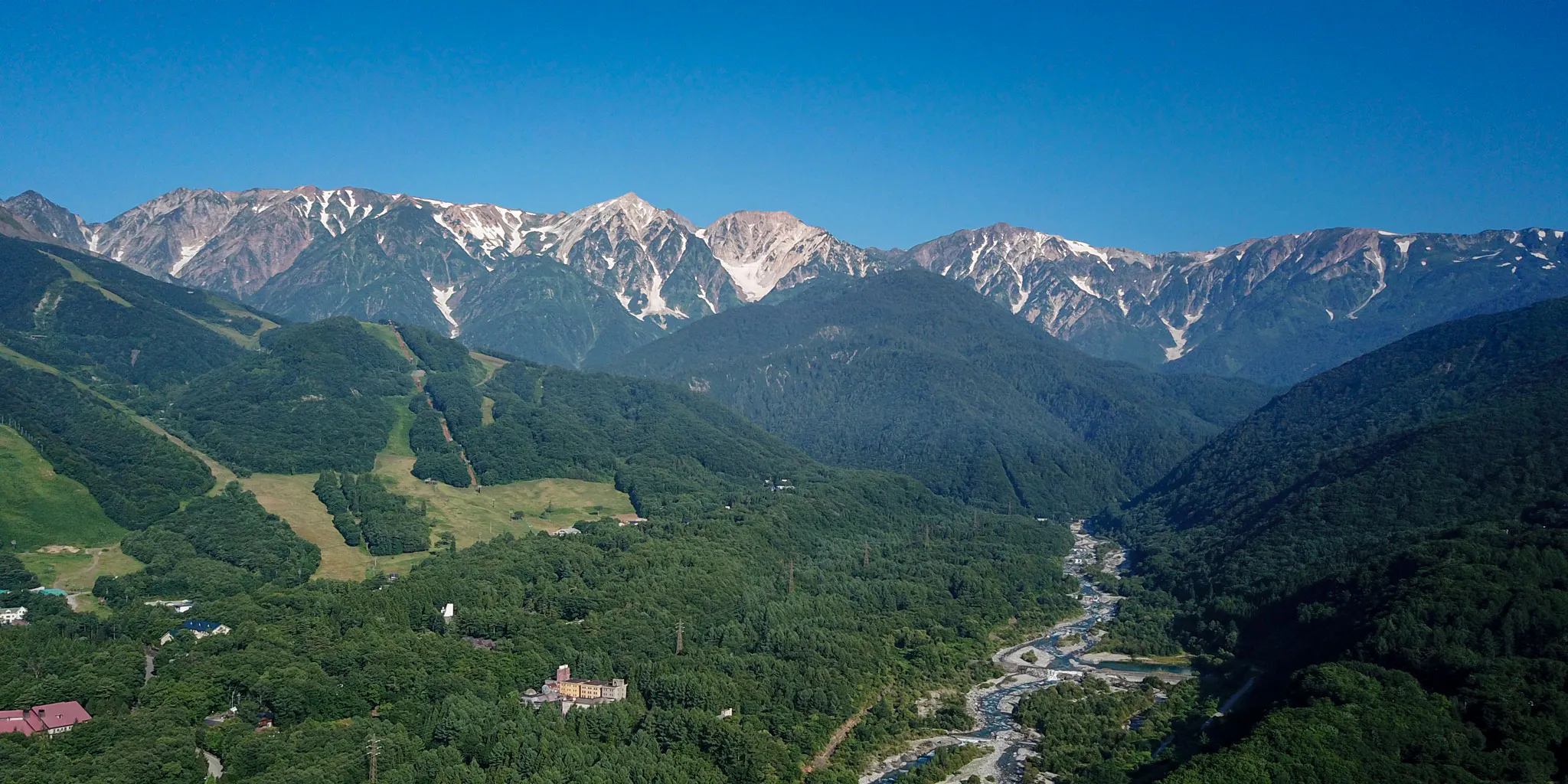 Aerial view of a mountain lodge and river valley with the Hakuba Sanzan range beyond