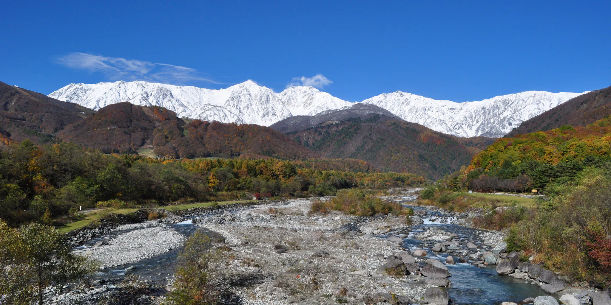 A river flowing through an autumn valley beneath the snow-capped Hakuba Sanzan