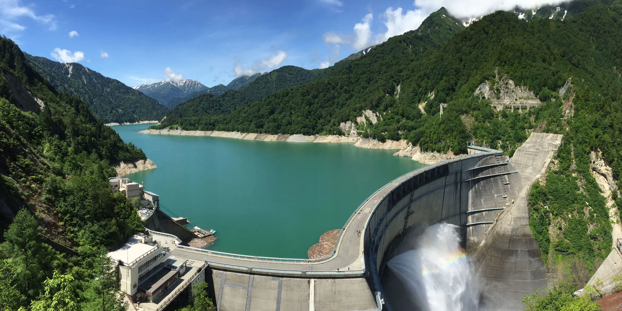 Kurobe Dam discharging water with a rainbow, surrounded by fresh green mountains