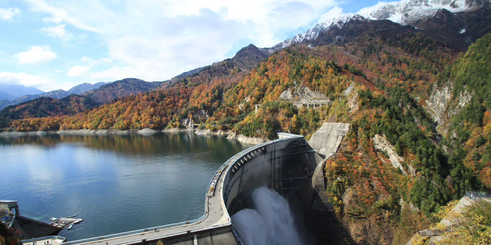 Kurobe Dam framed by autumn foliage, with snow-dusted mountains beyond