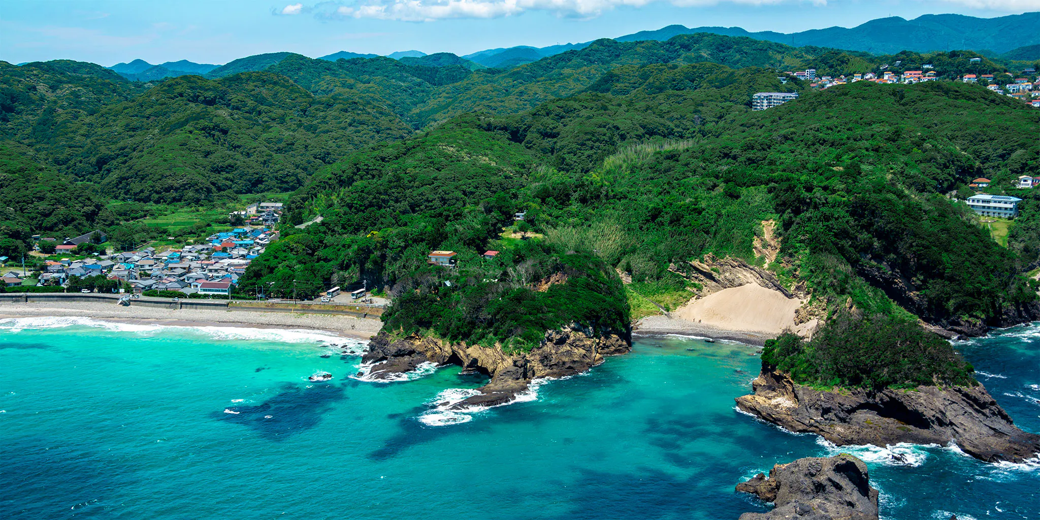 Aerial view of a sea arch and cove near Ryugukutsu, with turquoise water and a coastal village