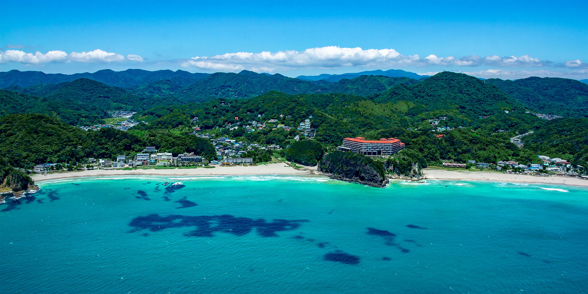 An orange-roofed hotel perched on a headland, surrounded by the cove's beach