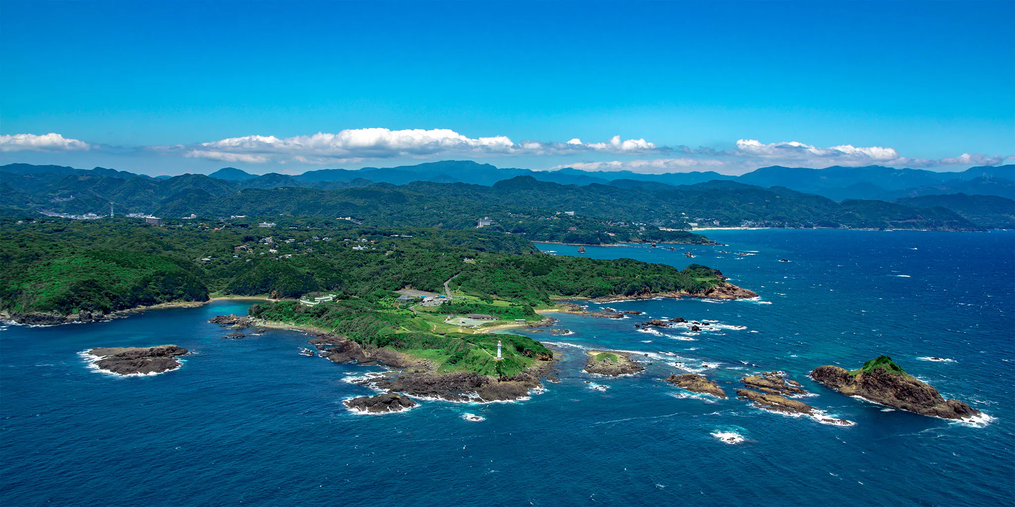 A wide aerial view of Tsumekizaki cape with its lighthouse and the Shimoda coastline beyond