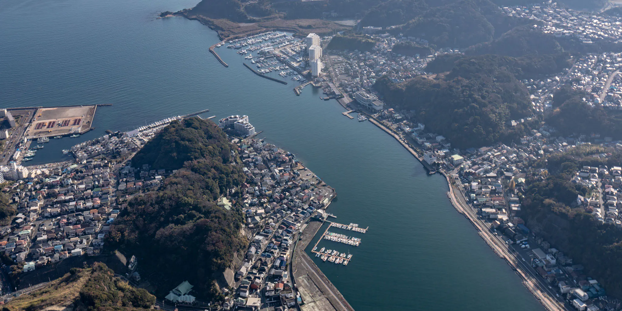 Aerial view of a narrow inlet channel with a fishing harbor, marina, and residential towns facing each other across the water