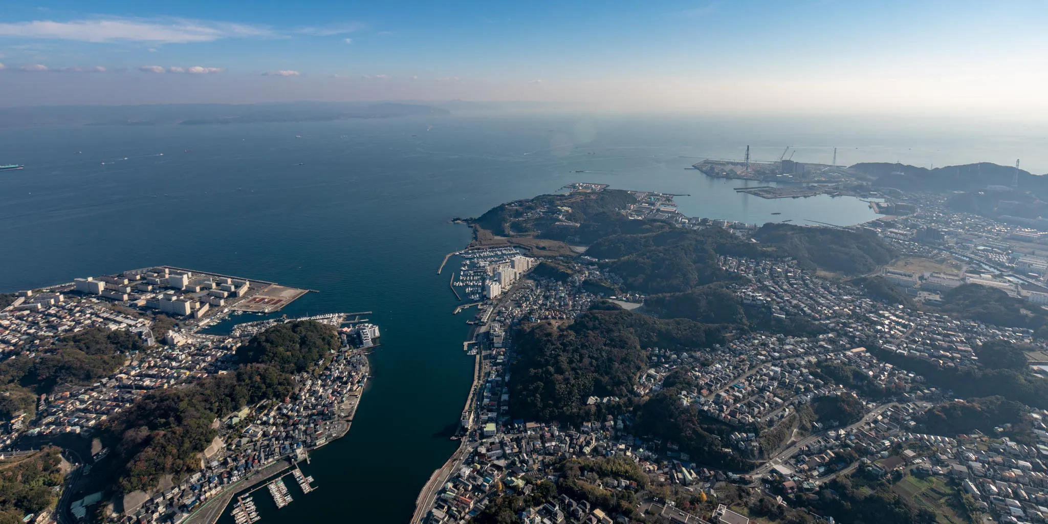 Aerial view of a bay with a marina in the foreground and industrial port cranes visible in the distance