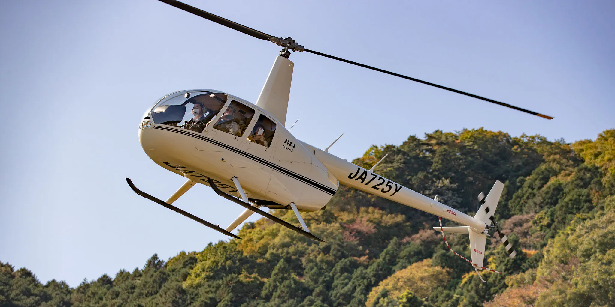 A Robinson R44 helicopter in flight over autumn-colored mountains