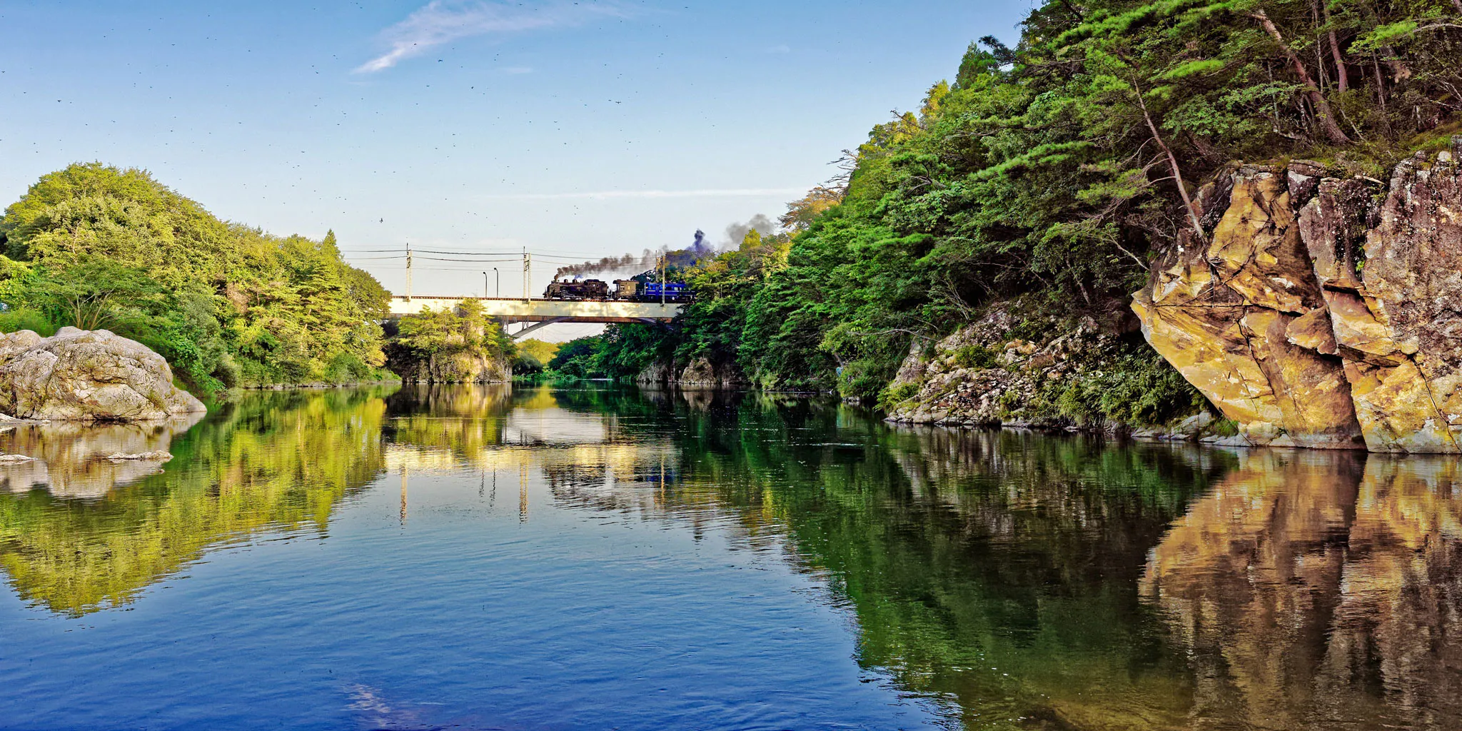 A steam train crossing a bridge over a rocky river gorge (Kinugawa Gorge)