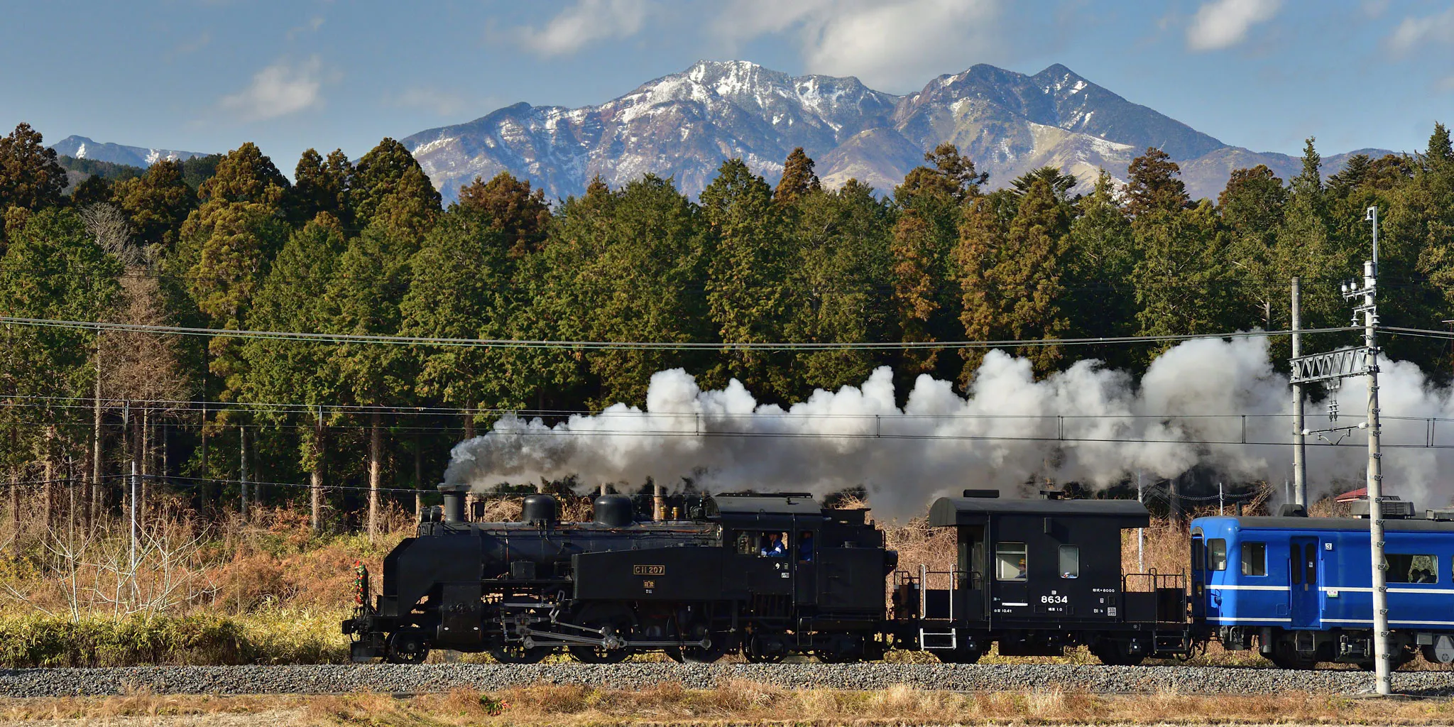 SL Taiju steam train with a blue passenger car, running with snow-capped mountains behind