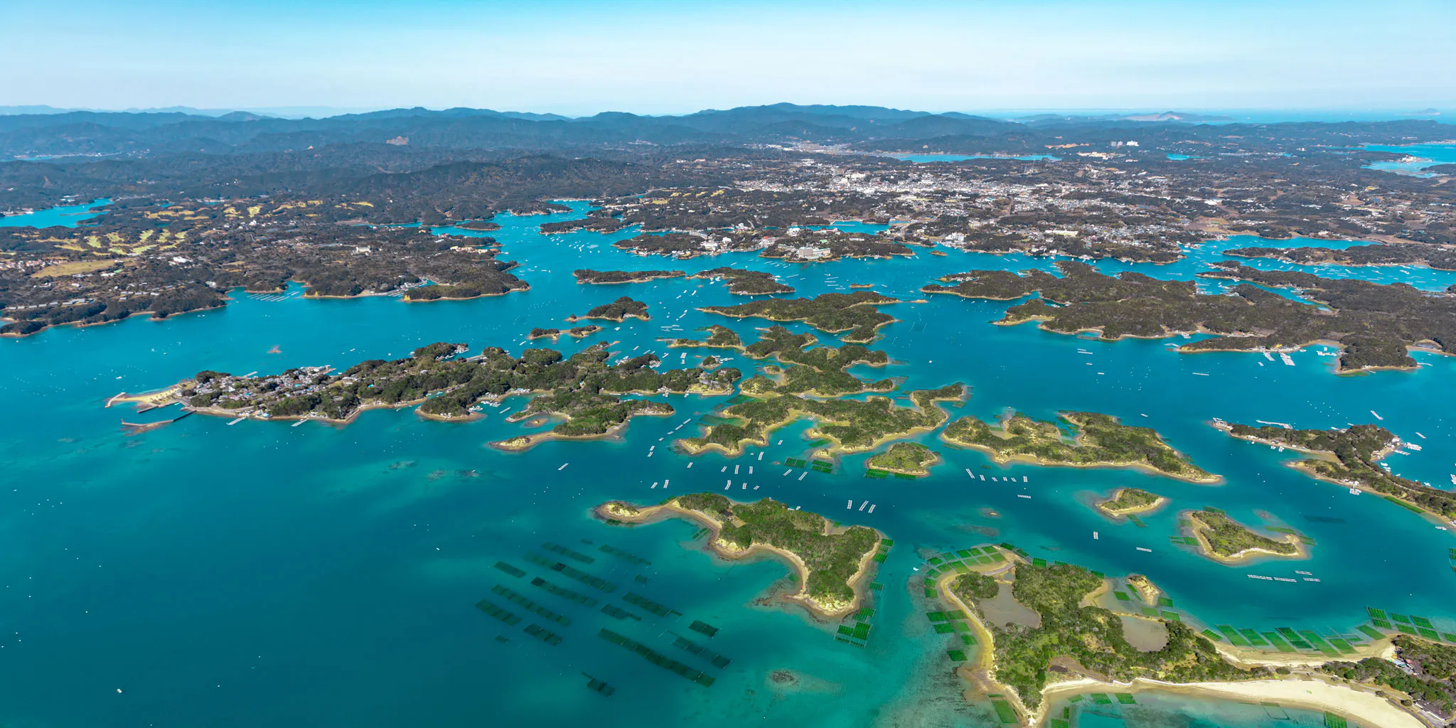Aerial view of a bay dotted with pearl farming rafts and numerous islands