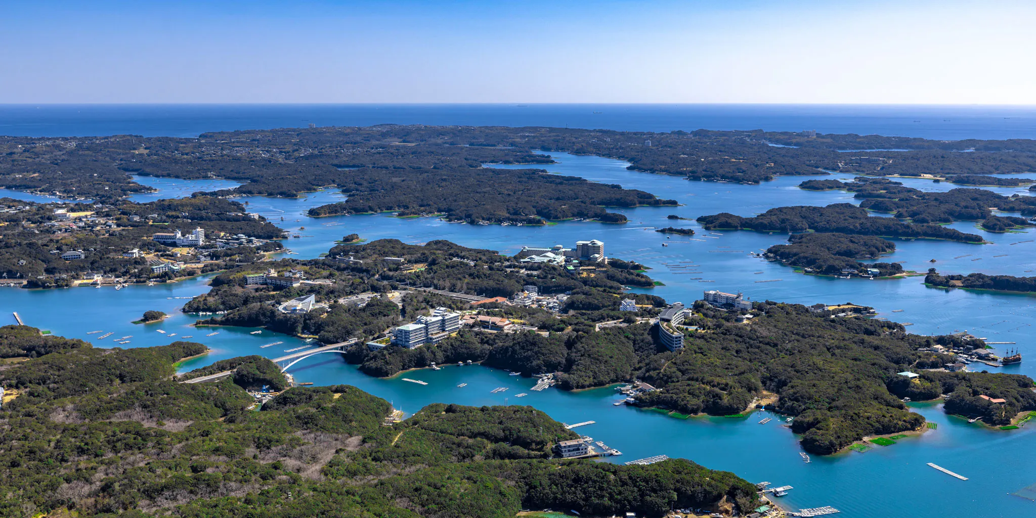 Aerial view of a bay with bridge-linked islands and large hotel buildings, likely near Kashikojima